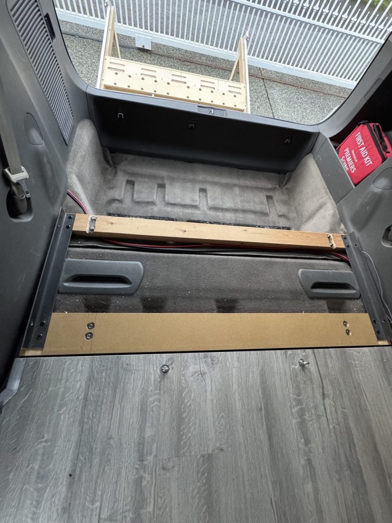 Lumber crossbars and steel angles bolted to the third-row seat strikers on the floor of a Toyota Sienna as the foundation for the camper bed frame