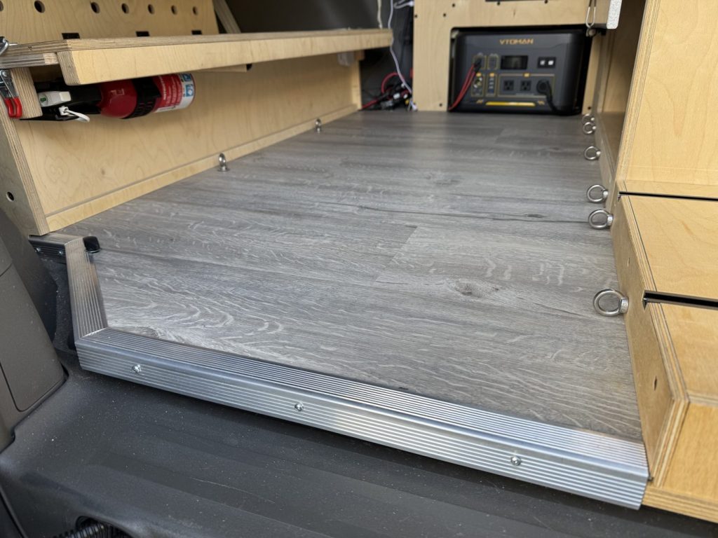 Finished grey vinyl tile floor in a minivan camper with aluminum edge trim, stainless eye bolts and plywood cabinet modules