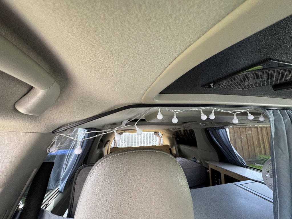Curtain rail bent to follow the ceiling headliner curve above the front seats of a Toyota Sienna minivan camper