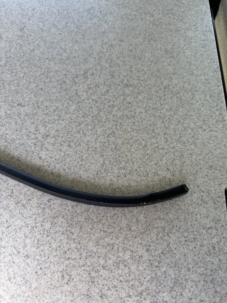 Black plastic self-adhesive curtain rail bent into a smooth curve, lying on a speckled grey countertop