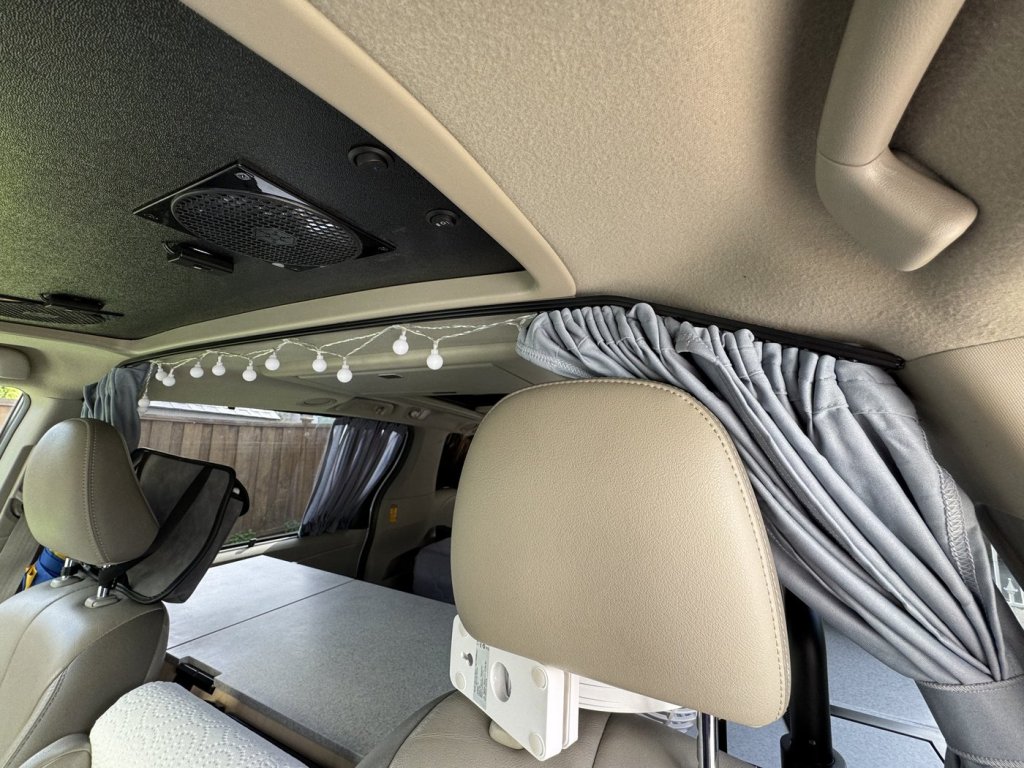 Black curtain rail glued along the sunroof frame in a Toyota Sienna minivan camper, with the grey divider curtain gathered at the side