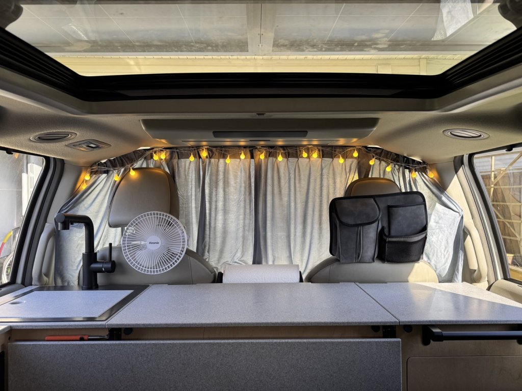 Grey divider curtain closed behind the front seats of a Toyota Sienna minivan camper, hanging from a rail under the sunroof frame