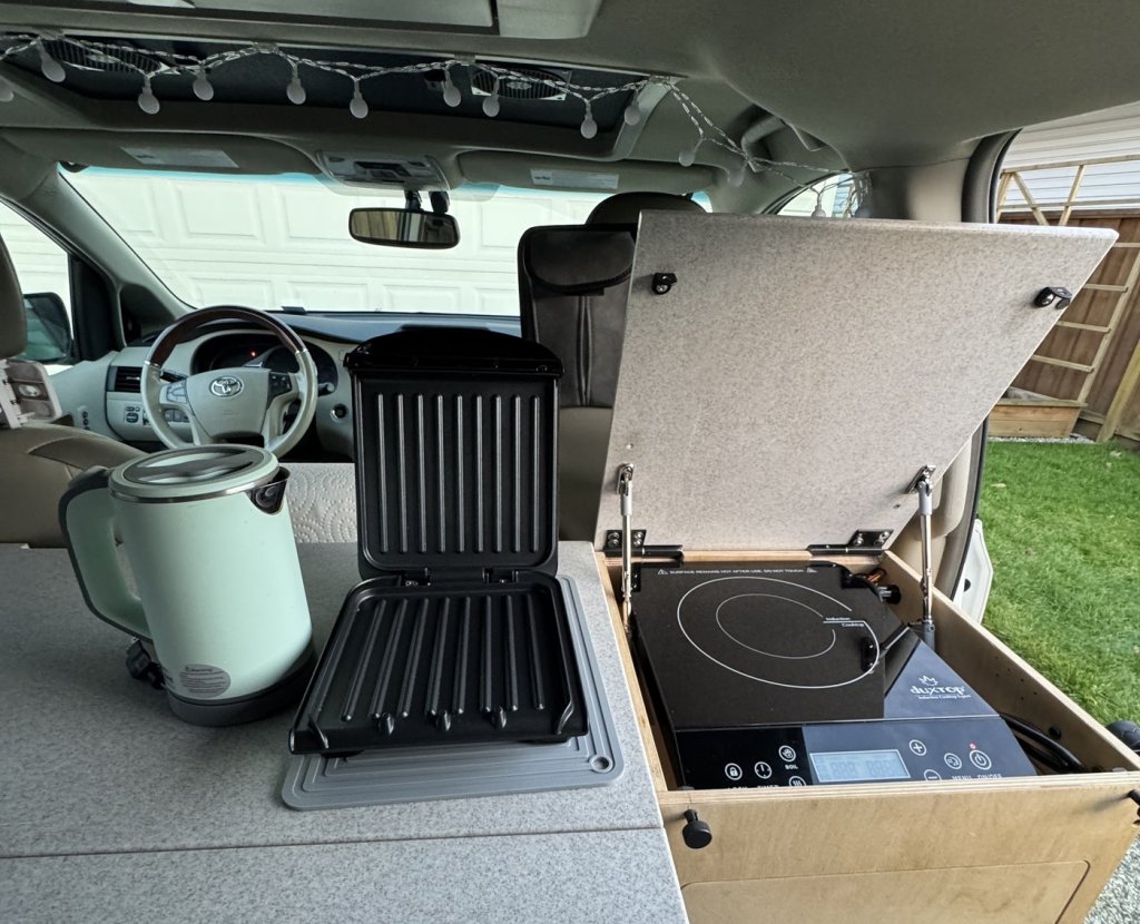 Electric kettle, panini press and Duxtop induction cooktop set up on the countertop inside a Toyota Sienna minivan camper