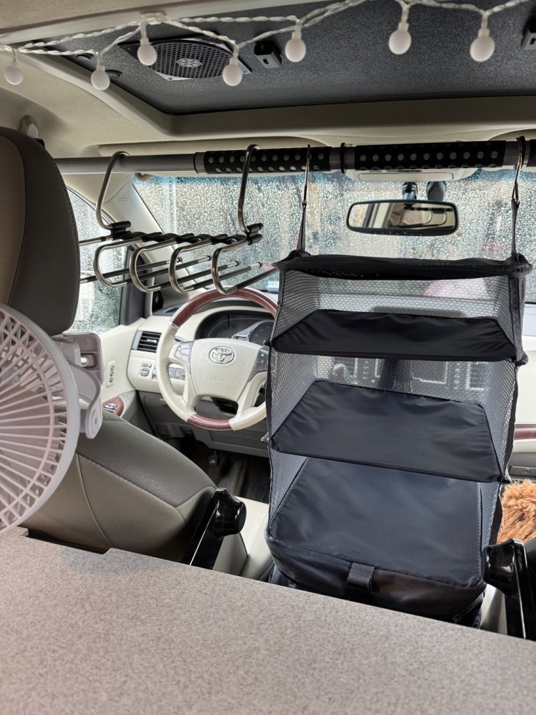 Hanging fabric shelf organizer and clothes rack on a rod above the front seats of a Toyota Sienna minivan camper