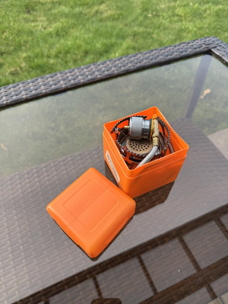 Compact backup camping stove with hose and gas adapter stored in a small orange plastic case