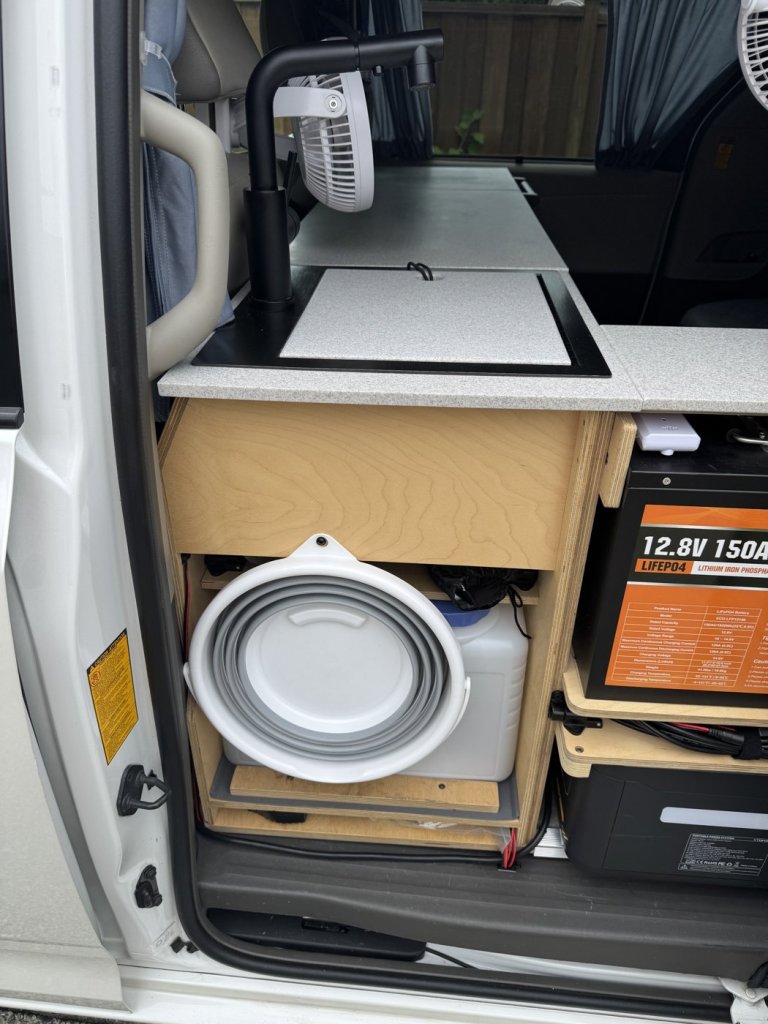 Birch plywood sink cabinet in a Toyota Sienna minivan camper with a Corian countertop, sink cutting board lid and open side for the water tanks