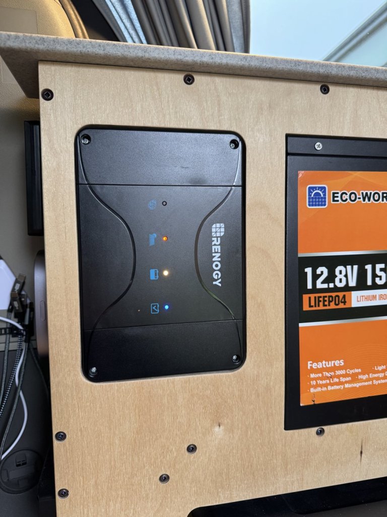 Renogy DCC30S charger controller mounted flush in a plywood cabinet next to the Eco-Worthy battery in a minivan camper