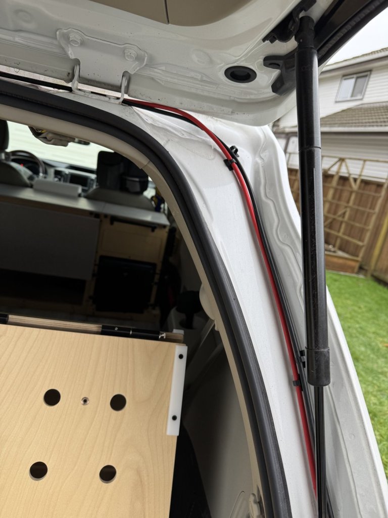 Red and black solar cables secured with clips along the rear hatch opening of a Toyota Sienna minivan camper